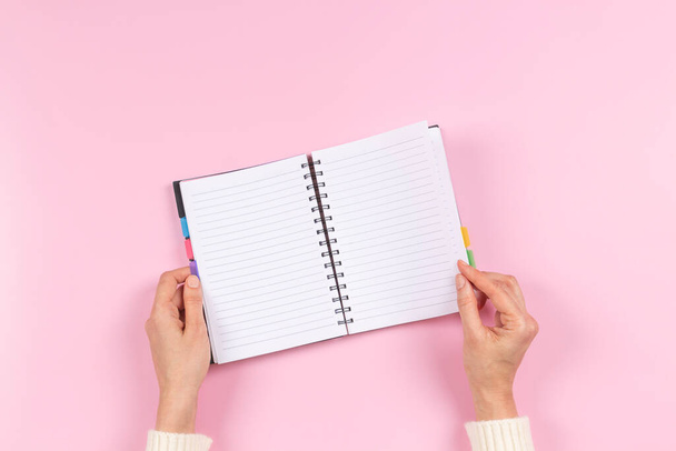 Manos femeninas sosteniendo en blanco cuaderno espiral abierto sobre fondo rosa pastel. Vista superior, espacio de copia. Educación, trabajo remoto, negocios, concepto financiero - Foto, imagen