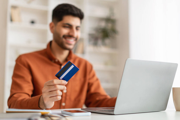 Lächelnder junger Mann mit PC und Kreditkarte, selektiver Fokus - Foto, Bild
