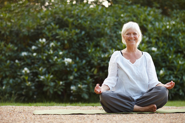 Doing her mindfulness exercises in the outdoors. Portrait of an attractive mature woman sitting in the lotus position outdoors. - Foto, Imagen