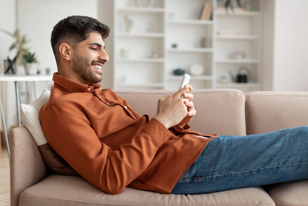 Portrét usměvavého Araba používajícího doma smartphone - Fotografie, Obrázek