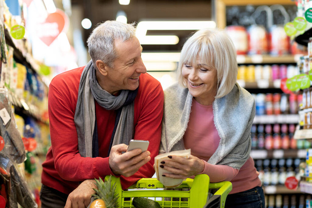 Feliz marido y esposa de edad avanzada de compras juntos, utilizando el teléfono inteligente - Foto, Imagen