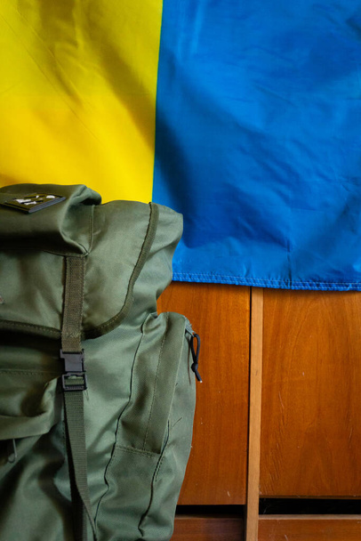 Στρατιωτικό σακίδιο. σημαία της Ουκρανίας στο παρασκήνιο. κοντινό πλάνο. - Φωτογραφία, εικόνα