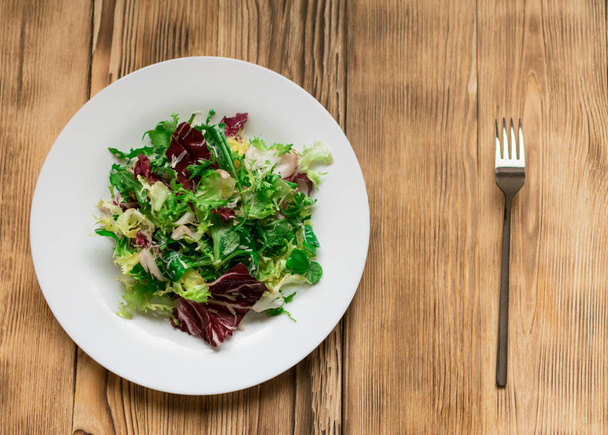 Vegetarian salad of fresh vegetables on a white plate on a wooden background. - Fotó, kép