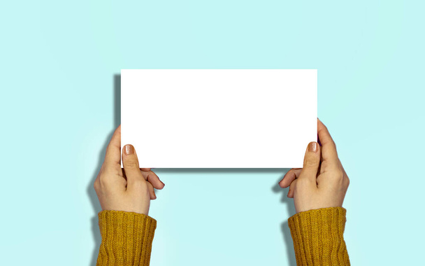 manos de mujer de primer plano sosteniendo un papel en blanco, cartelera para su diseño o logotipo o texto - Foto, Imagen