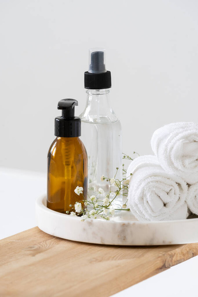 Set of glass cosmetic bottles and towels on white background. Bath accessories usage. Home spa concept. Body treatment. Healthy cosmetology. Natural beauty products - Photo, image