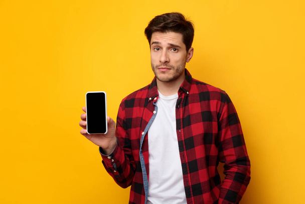 Sad guy holding showing empty smartphone screen - 写真・画像