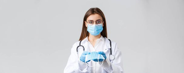 Covid-19, prevence viru, kliniky, zdravotnických pracovníků a koncepce karantény. Mladý lékař v lékařské masce a rukavicích, bílé pláště, poskytující ochranu obličeje pacientům, vypadat vážně - Fotografie, Obrázek