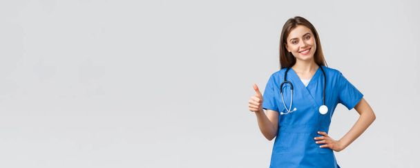 Medical workers, healthcare, covid-19 and vaccination concept. Attractive cheerful female nurse, doctor in scrubs showing support, recommend or advice medicine, show thumbs-up in approval smiling - Photo, Image
