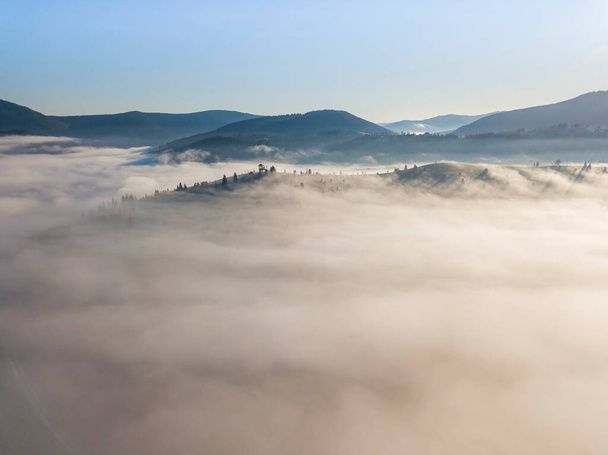 Vuelo sobre niebla en los Cárpatos Ucranianos en verano. Montañas en el horizonte. Una gruesa capa de niebla cubre las montañas con una alfombra continua. Vista aérea del dron. - Foto, imagen