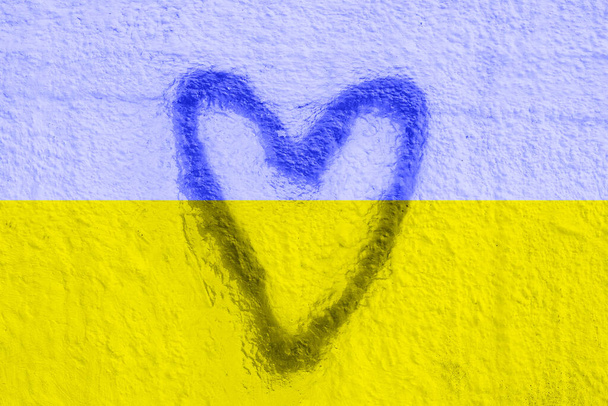El símbolo de la bandera nacional de Ucrania en forma de corazón en un muro de hormigón agrietado. Concepto. - Foto, imagen