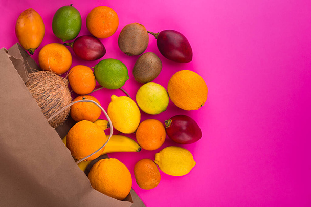 Zitrusfrüchte auf rosa Hintergrund. Verschiedene Zitrusfrüchte und Tamarillo. Kiwi auf rosa Tisch und andere Früchte. Kopieren Sie Platz für Ihren Text. Früchte aus Papiertüte auf der linken Seite. - Foto, Bild