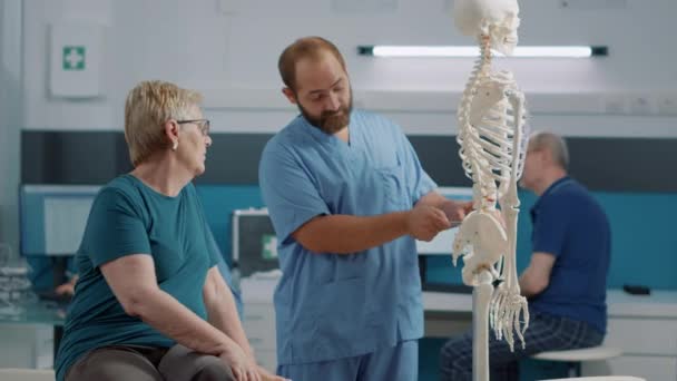 Férfi osteopatha magyarázó hátfájás az emberi csontváz csontok - Felvétel, videó