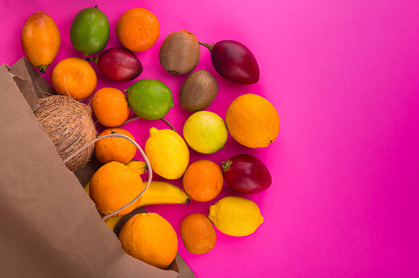 Citrusvruchten op rozen achtergrond. Diverse citrusvruchten en tamarillo. Kiwi op roze tafel en andere vruchten. Kopieer ruimte voor je tekst. Vruchten van papieren zak aan de linkerkant. - Foto, afbeelding
