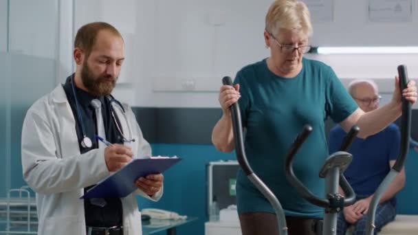 Lékař dává rady starší ženě na stacionárním kole - Záběry, video