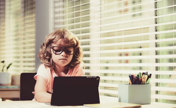 Kid at online school, home schooling. Distance learning. Cheerful little boy using laptop tablet studying through online e-learning system. - 写真・画像