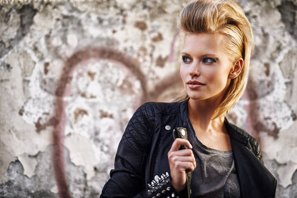Rocknroll fashion. An edgy young woman holding the collar of her leather jacket. - Φωτογραφία, εικόνα
