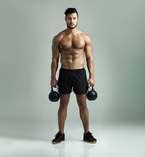 Serious about staying in shape. Studio shot of a young man working out with kettle bells against a gray background. - Φωτογραφία, εικόνα