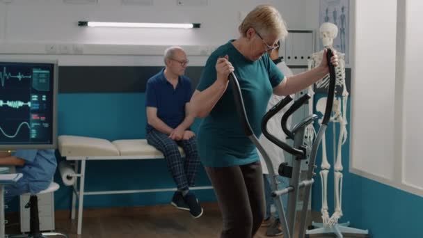 Muotokuva vanhempi nainen tekee fysioterapiaa paikallaan polkupyörän - Materiaali, video