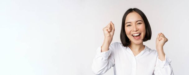 De cerca retrato de la cara de la mujer asiática bailando sonriendo, triunfando y celebrando con emoción feliz, de pie sobre fondo blanco - Foto, Imagen