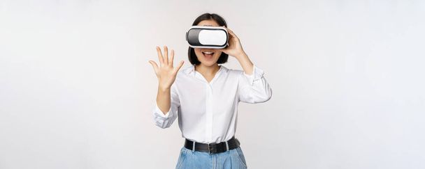 Συζήτηση VR. Ασιάτισσα κοπέλα λέει γεια σε γυαλιά εικονικής πραγματικότητας, χαμογελώντας ενθουσιώδης, έννοια της επικοινωνίας και της μελλοντικής τεχνολογίας, λευκό φόντο - Φωτογραφία, εικόνα