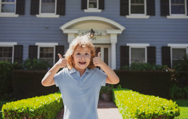 Close up head shot of child outdoor home with thumbs up sign, near house. Kids face, little boy portrait. - Φωτογραφία, εικόνα