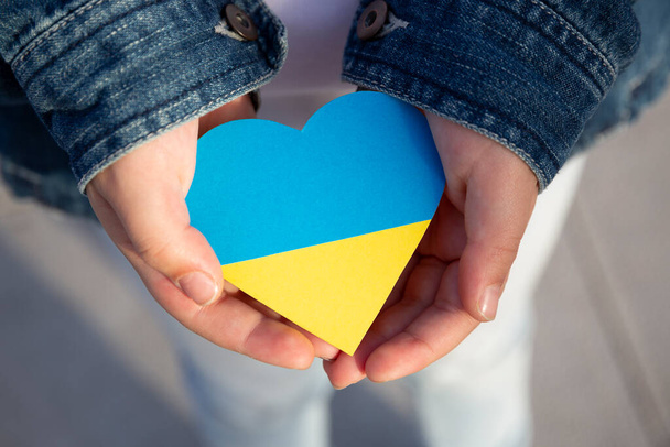 Primer plano de las manos de un niño pequeño sosteniendo un corazón en los colores de la bandera ucraniana que muestra apoyo y solidaridad. Protesta contra la invasión rusa. - Foto, imagen