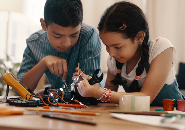 El futuro está en buenas manos. Tiro de dos adorables hermanos jóvenes construyendo un coche de juguete robótico juntos en casa. - Foto, imagen
