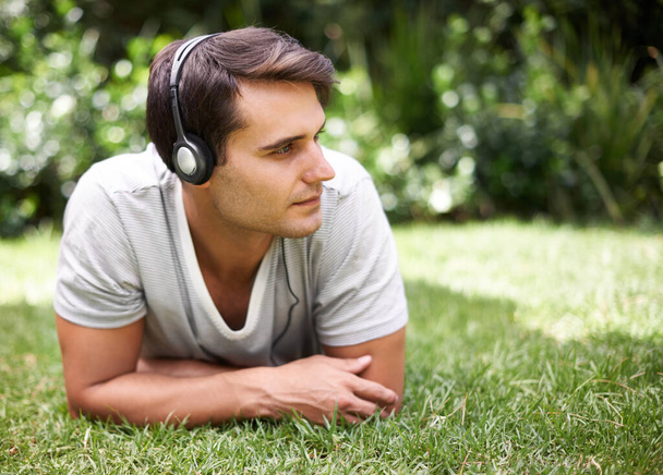 Zoning out with my headphones. Shot of a handsome young man listening to music while lying outdoors. - Fotoğraf, Görsel