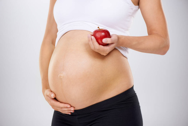 Dieta saludable para el bebé. Imagen recortada de una mujer embarazada sosteniendo una manzana y tocándose el estómago amorosamente. - Foto, Imagen