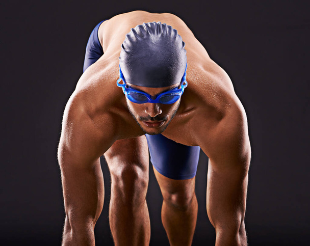 Haz que las vueltas cuenten. Captura de estudio de un apuesto nadador listo para zambullirse en el bloque de salida. - Foto, Imagen