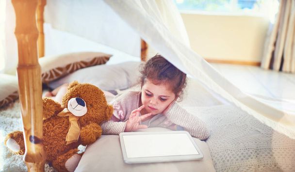 Zelfs kleine kinderen weten tegenwoordig zoveel over technologie. Shot van een schattig klein meisje met behulp van een digitale tablet thuis. - Foto, afbeelding