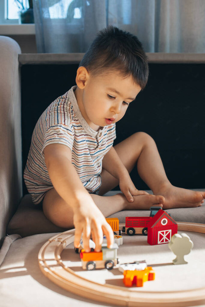 Caucasian little boy playing with wooden train while sitting on floor, building toy railroad at home. - Fotografie, Obrázek