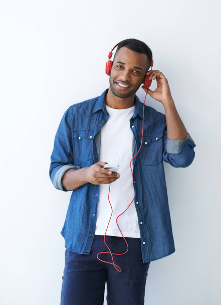Genießen Sie diese Strecke. Ein junger afrikanisch-amerikanischer Mann trägt Kopfhörer und hört Musik vor weißem Hintergrund. - Foto, Bild