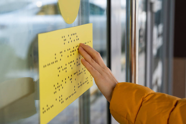 Close-up of a woman reading a braille lettering on a glass door. - Фото, зображення