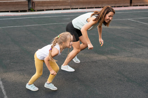 Caucasian woman goes in for sports with her daughter outdoors. A schoolgirl and her mother are running around in the stadium. - Foto, imagen