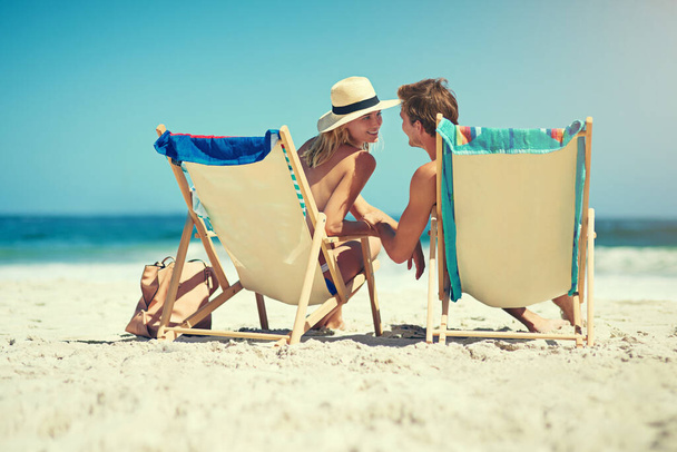 Simplemente no sería lo mismo sin ti. Vista trasera de una joven pareja sentada en tumbonas en la playa. - Foto, imagen