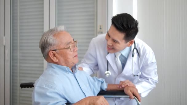 Cuidar a un médico asiático apoyando y animando a un paciente masculino mayor durante la visita. Terapeuta y anciano hombre de pelo blanco, comunicando y discutiendo el tratamiento - Imágenes, Vídeo