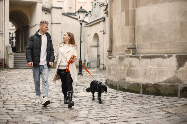 Lovely couple holding hands while walking with their dog in the street of old town - Fotó, kép