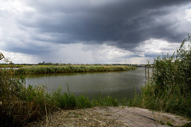 Paysage rural avec côte fluviale, roseau et ciel nuageux - Photo, image