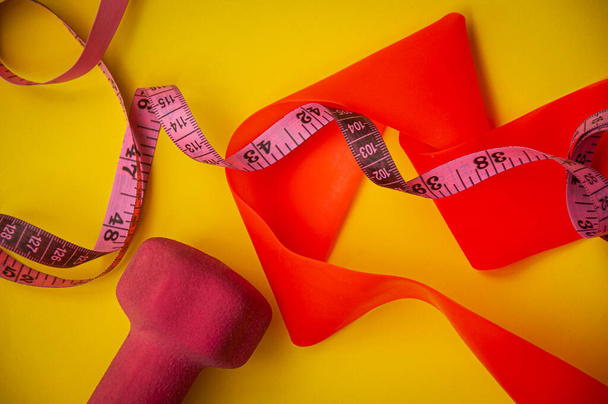 Hantel, Gummizug und Maßband von oben auf gelbem Hintergrund - Fitness- und Gewichtsreduktionskonzept - Foto, Bild