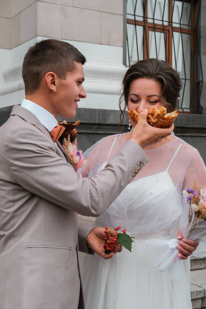 Happy young bride feeding wedding cake to groom outdoors. Weeding traditions. Lovely couple feed each other - Photo, Image