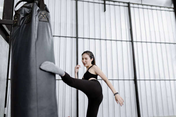 conceito de exercício A mulher de boxe sendo concentrada em bater o saco de boxe pesado por uma de suas pernas. - Foto, Imagem
