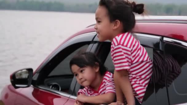 Aranyos ázsiai testvérek lányok mosolyognak, és szórakozás utazik autóval, és néz ki az autó ablakán. Boldog család élvezi utazás a nyári vakáció. - Felvétel, videó