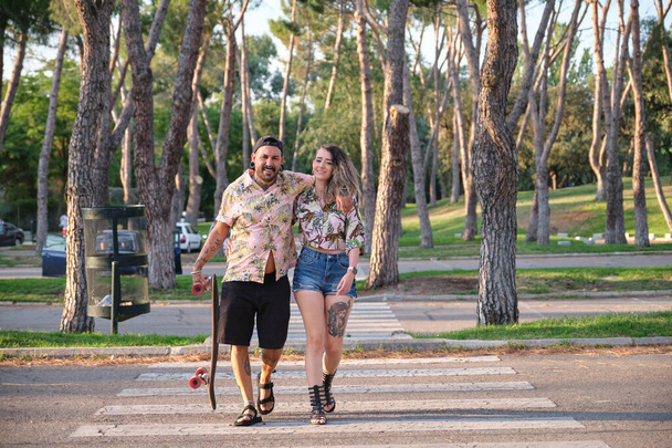 Joven pareja tatuada fresca caminando junto con un longboard. - Foto, Imagen