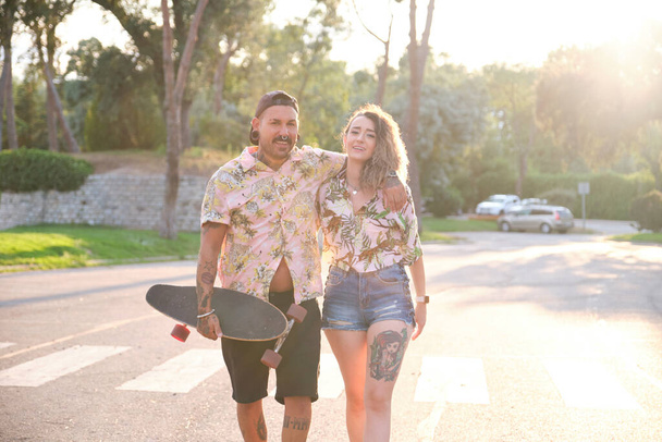 Young cool tattooed couple walking together with a skateboard. - Photo, Image