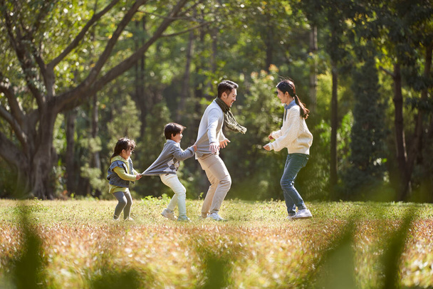 молода азіатська сім'я з двома дітьми розважається граючи в гру на відкритому повітрі в парку
 - Фото, зображення