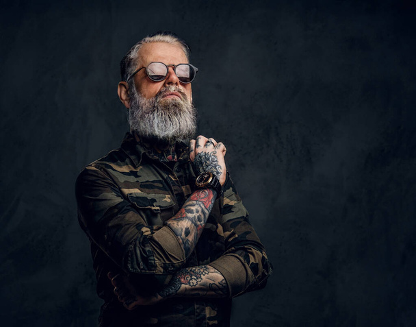 Stylish grandfather with sunglasses and crossed arms against dark background - Фото, изображение
