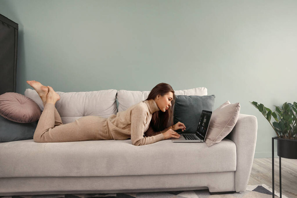 Beautiful young woman working with laptop on couch. Businesswoman using laptop managing her business. Communicates on internet.  - Фото, изображение