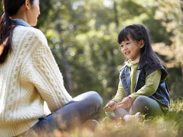 都会の公園で会話を楽しむ若いアジア系の母親と娘 - 写真・画像