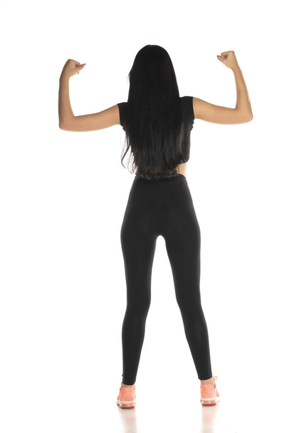 Rear view of beautiful young sporty woman standing on white background and showing her arms - Photo, Image